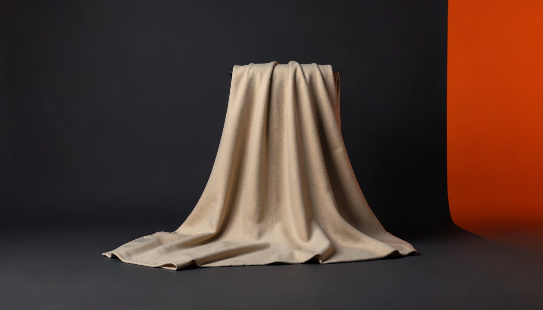 A calm studio scene in soft charcoal and warm tan tones, a single draped textile lit gently against a seamless dark backdrop, evoking a quiet editorial mood