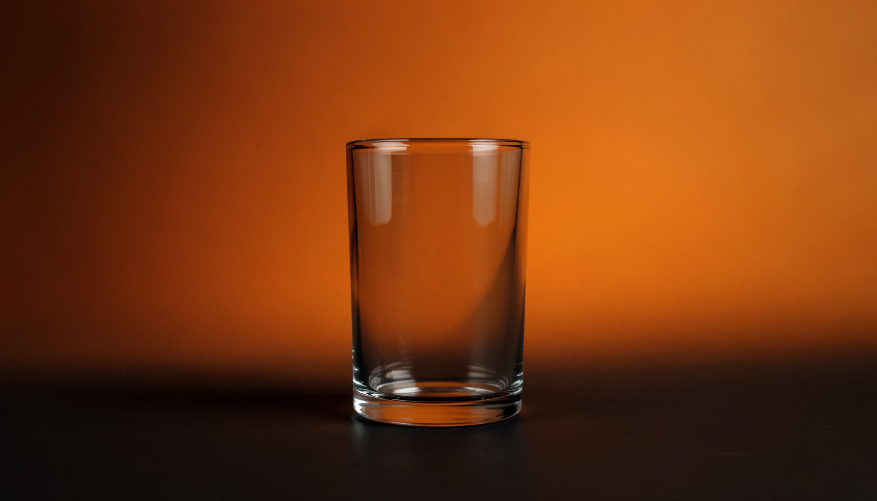 A single glass object catching soft light on a dark seamless studio backdrop, warm tan and near-black tones, restrained and gallery-like